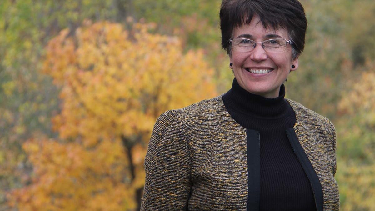 Image of Emmaus CEO Karen Jacobsen in front of fall leaves.